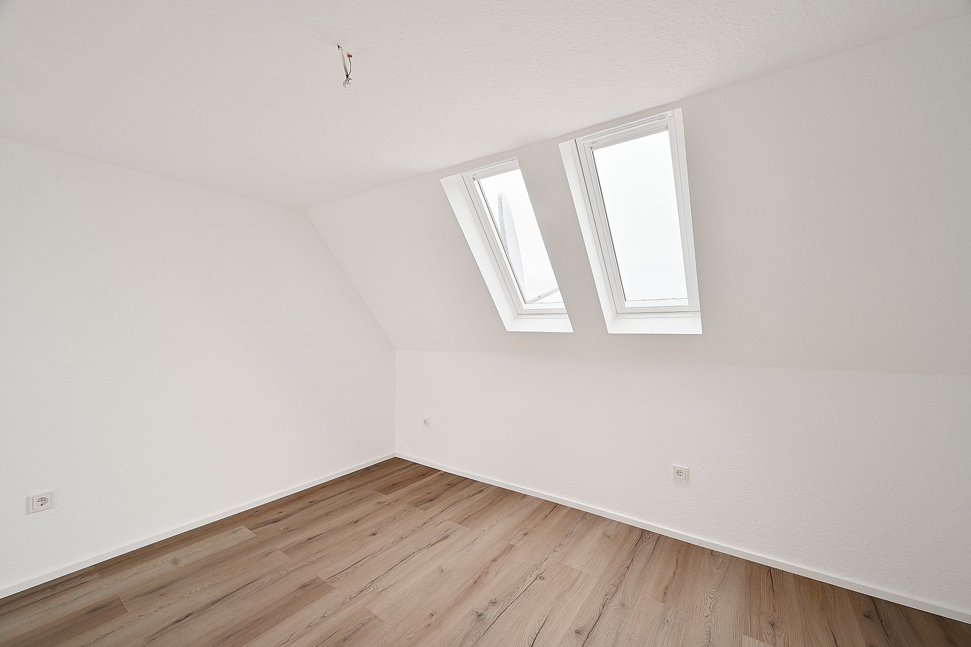 Leerer Raum mit Dachschräge, zwei Dachfenstern und Holzfußboden.