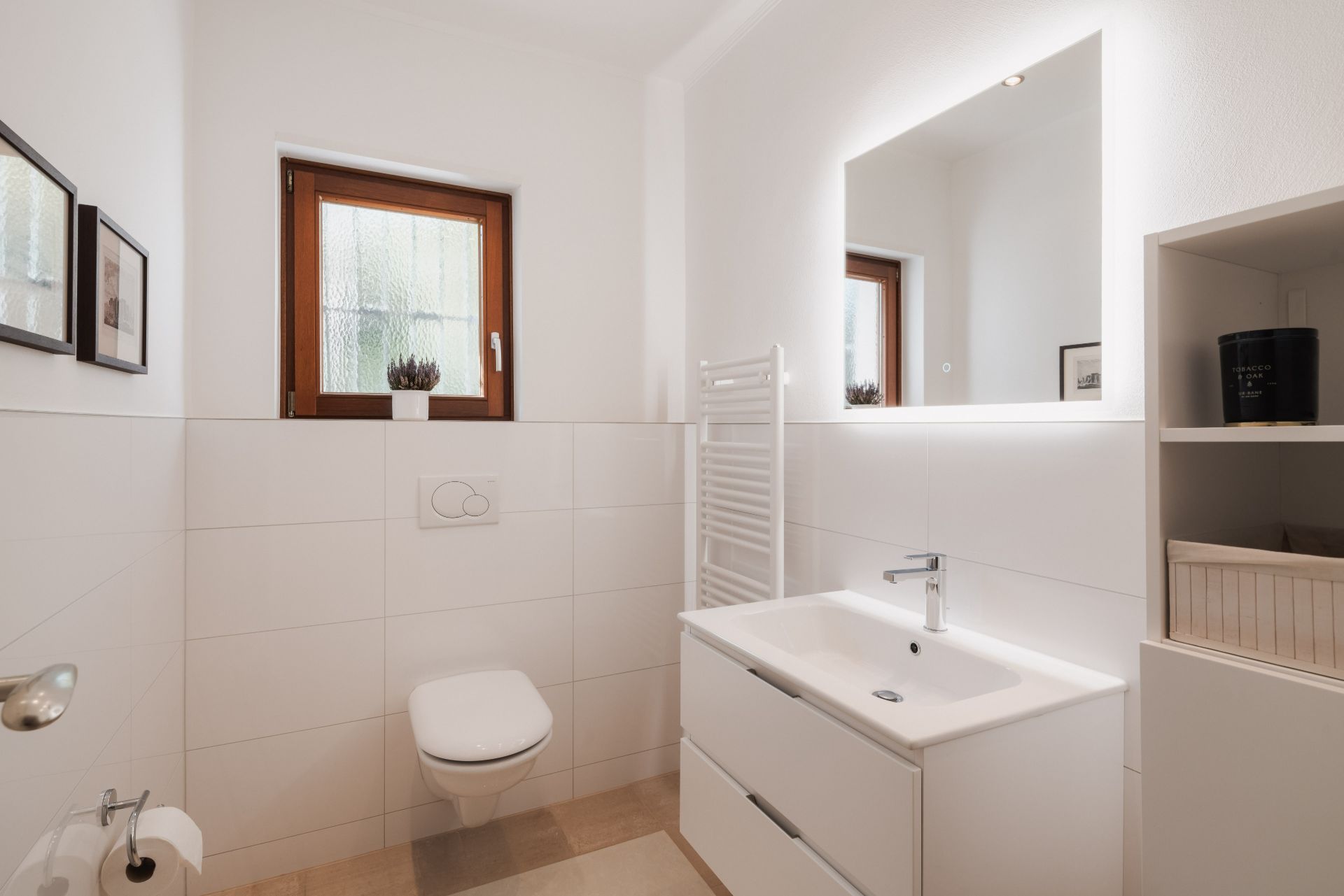 Modernes Badezimmer mit Wand-WC, Waschbecken, Spiegel, Fenster und Handtuchheizkörper.