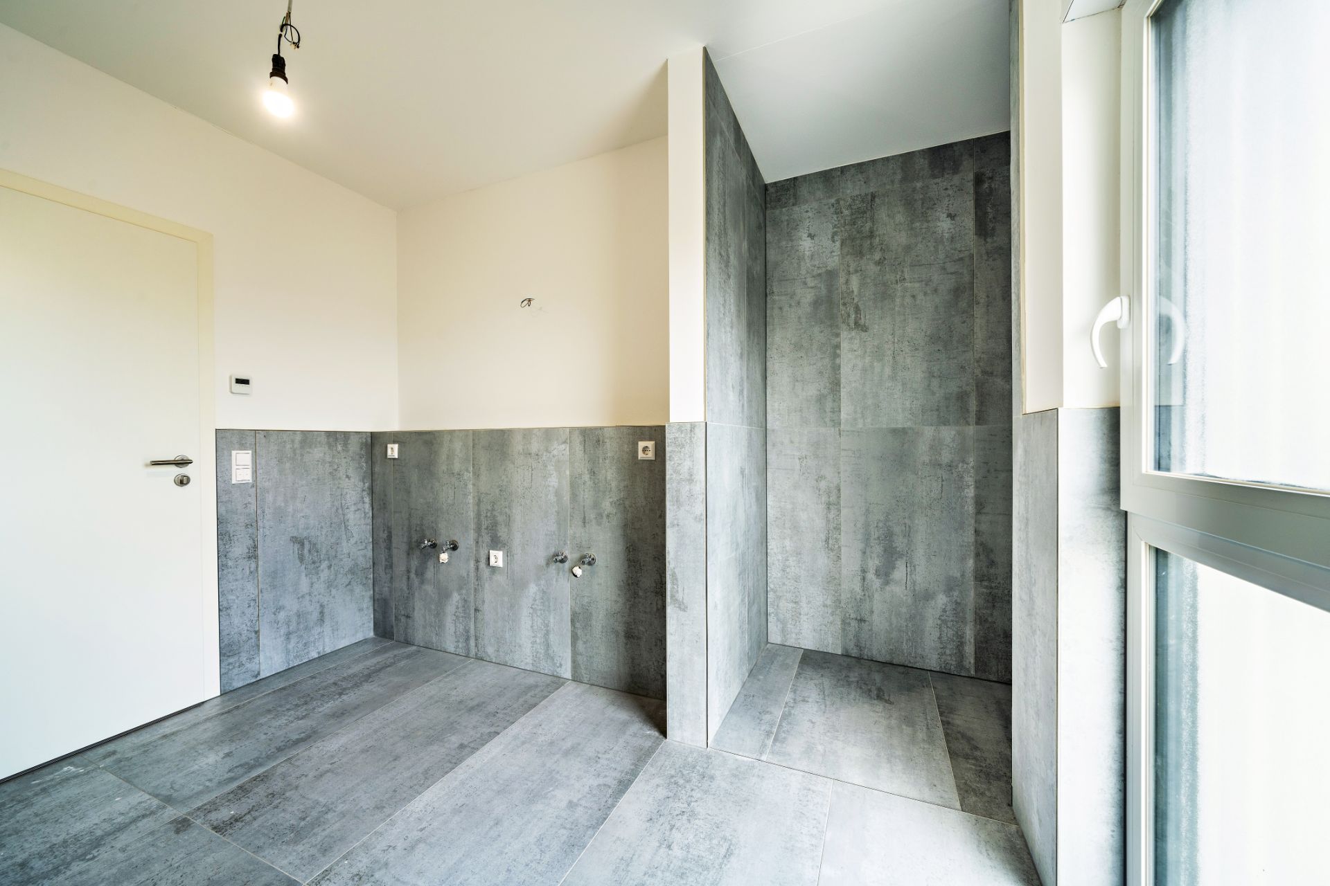 Modernes, leeres Badezimmer mit grauen Fliesen und einer offenen Dusche.