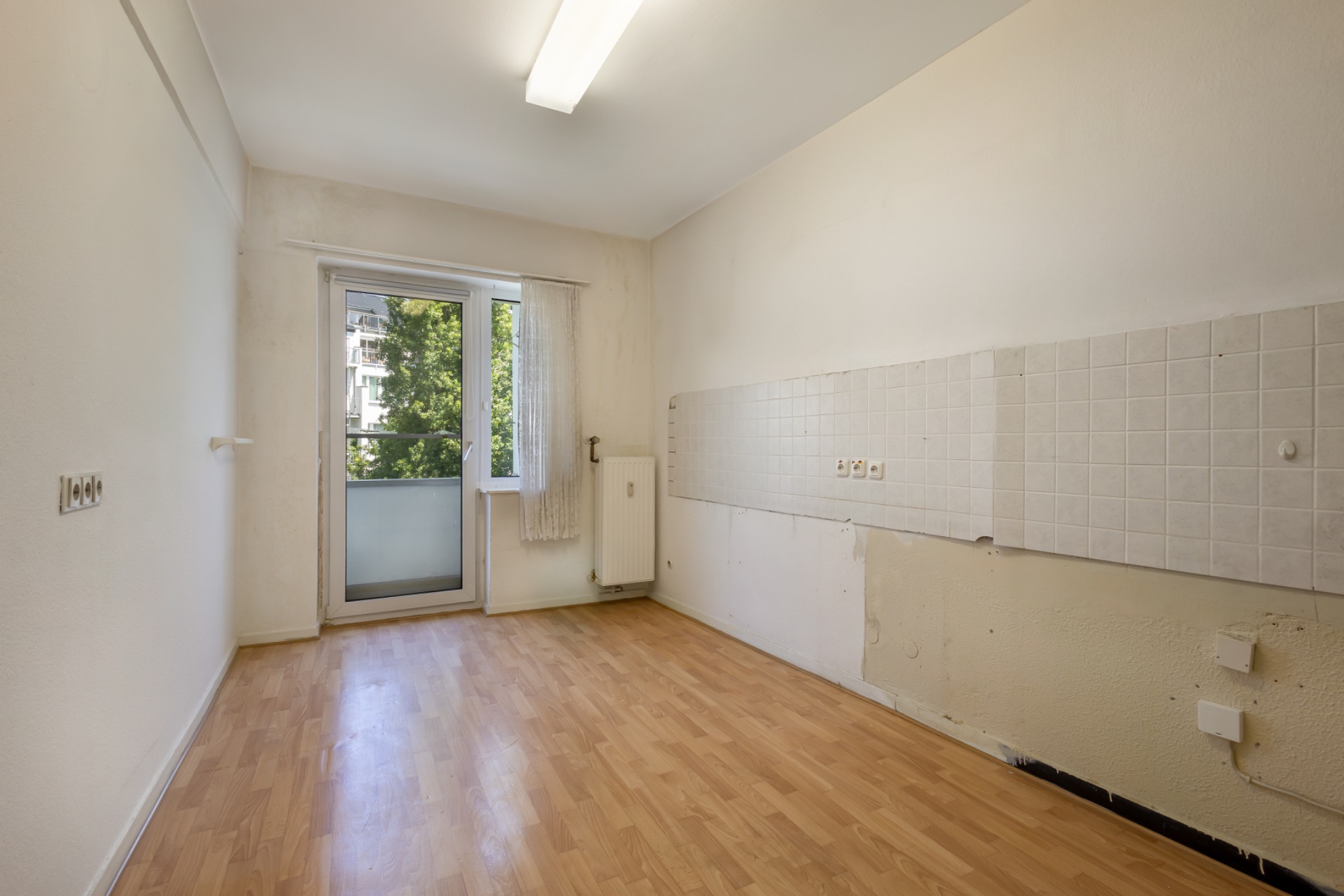 Leerer Raum mit Laminatboden, weißer Wand, Fenster und Tür zum Balkon.