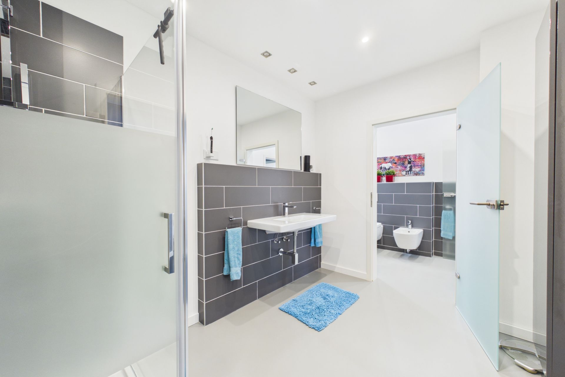 Modernes Badezimmer mit Dusche, Doppelwaschbecken, Handtüchern und Blick auf ein separates WC.