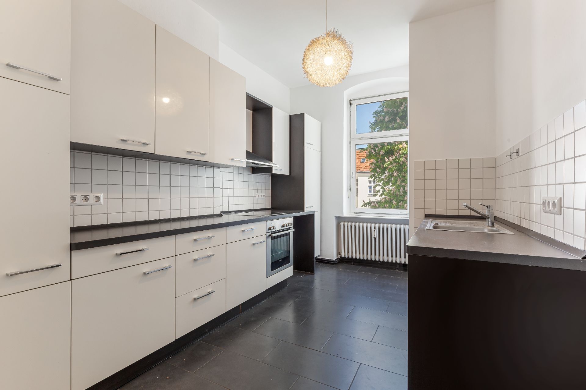 Moderne Einbauküche mit weißen Schränken, Herd, Spüle und großem Fenster.