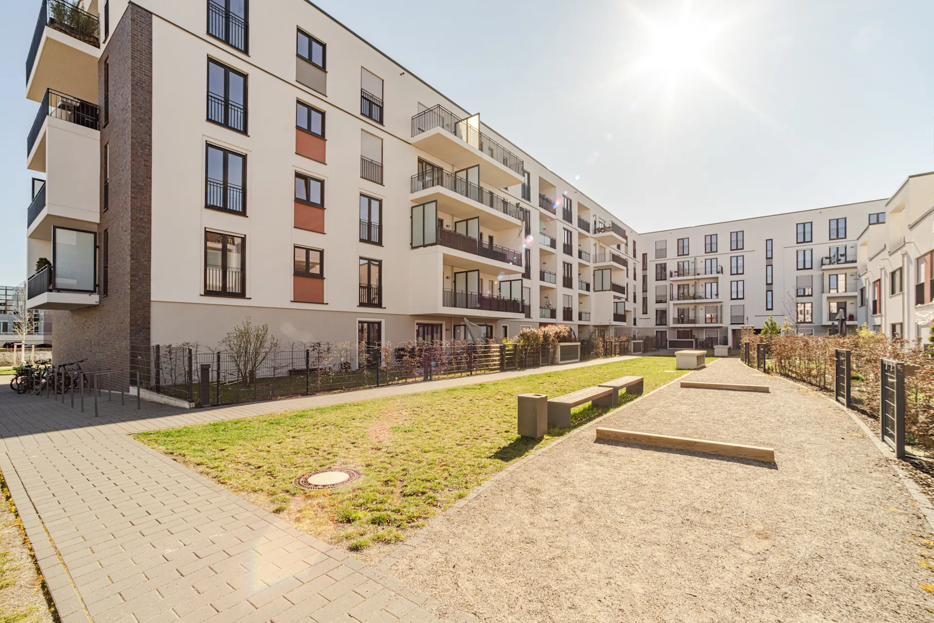 Moderner Innenhof mit Sitzbänken, gepflasterten Wegen und Wohngebäuden im Hintergrund.