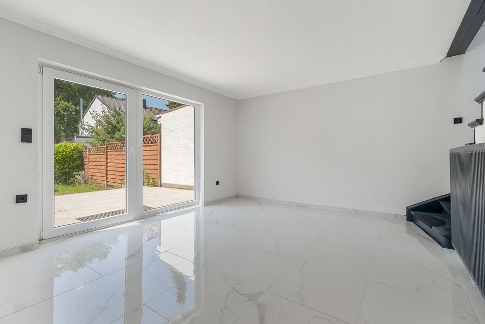Helles Wohnzimmer mit großen Fenstern, Fliesenboden und Blick auf den Garten.