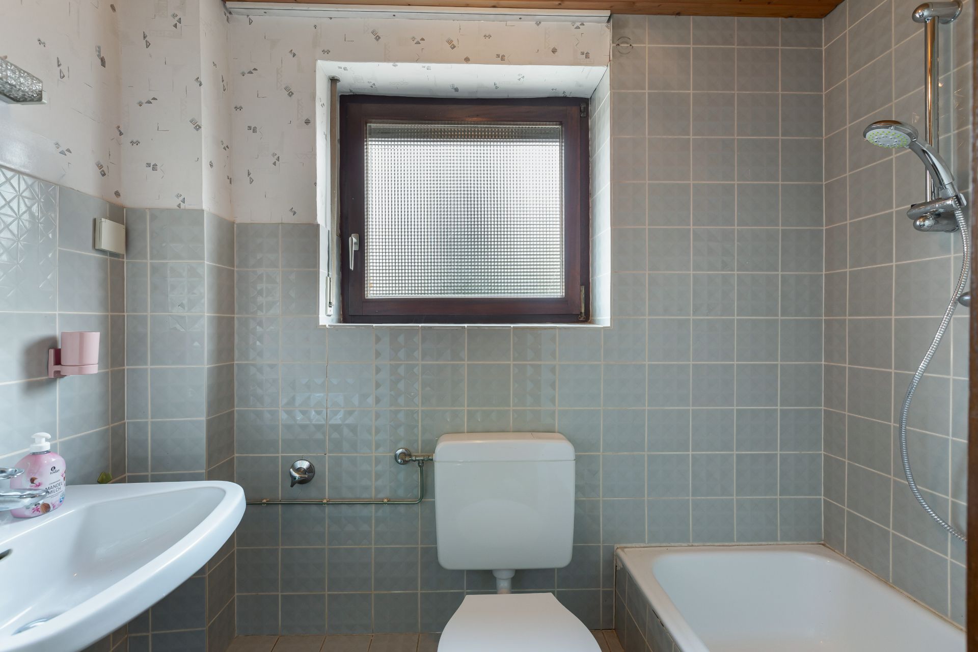 Kleines Badezimmer mit Toilette, Waschbecken, Badewanne und Fenster mit Milchglas.