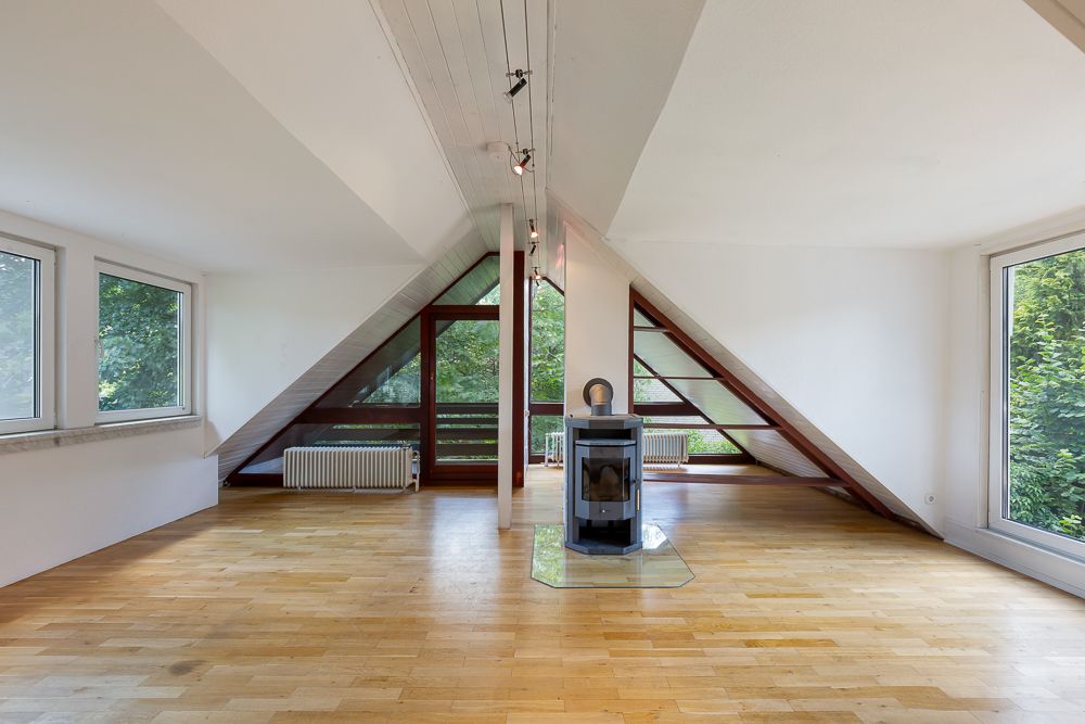 Helles Wohnzimmer mit Holzboden, großen Fenstern und Kamin unter einem schrägen Dach.