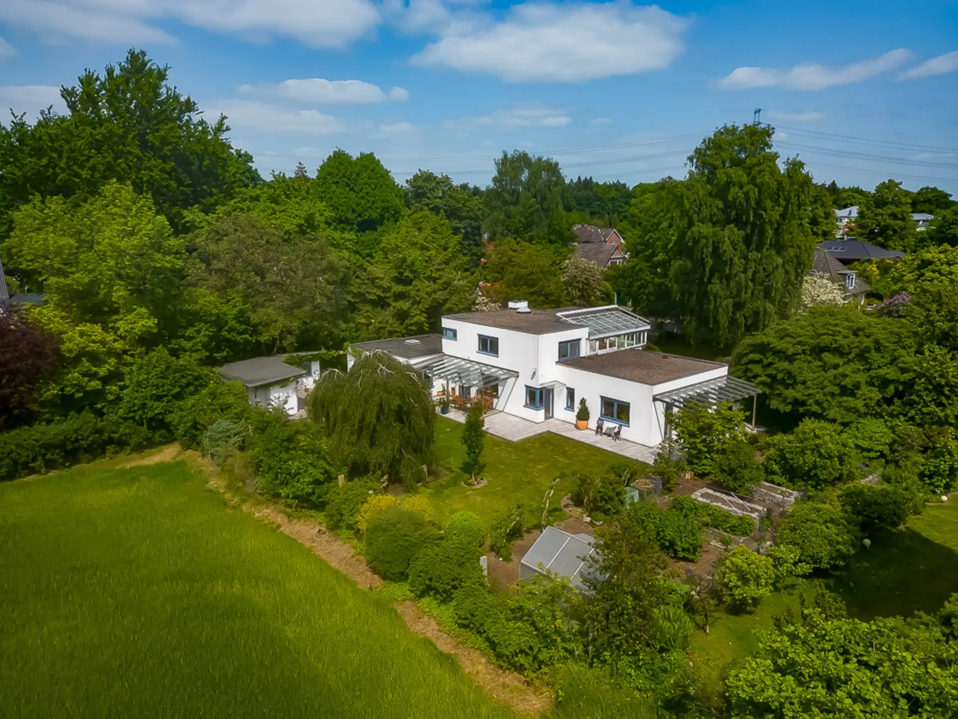 Modernes Einfamilienhaus mit Flachdach, Garten und viel umliegendem Grün, aus der Vogelperspektive gesehen.