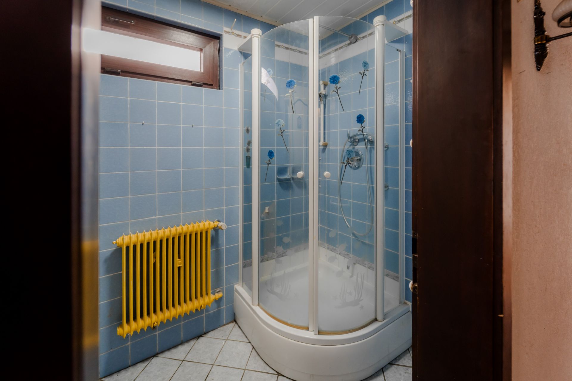 Badezimmer mit blauen Fliesen, Dusche mit Glastüren und gelbem Heizkörper.