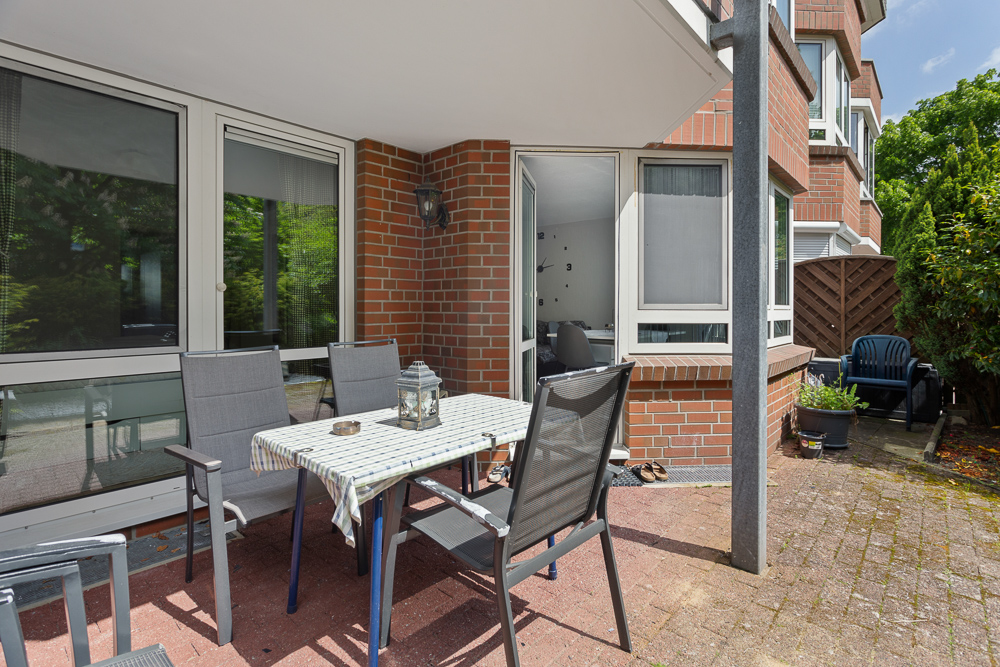 Terrasse mit Tisch, vier Stühlen, Pflanzkübeln und Zugang zur Wohnung, umgeben von Ziegelwänden.