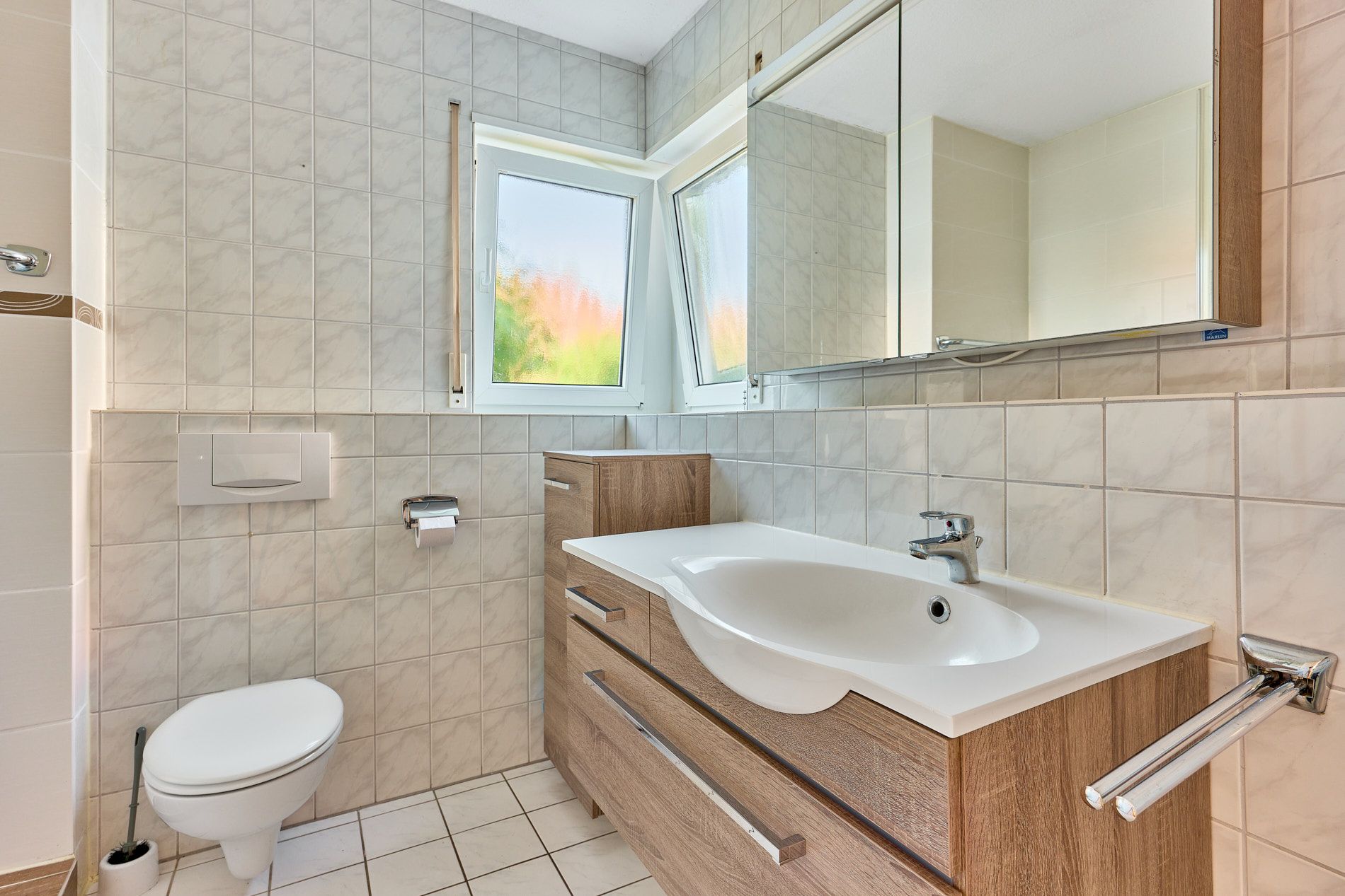 Modernes Badezimmer mit WC, Waschbecken, Holzunterschrank und großem Spiegel, Fenster zur Seite.