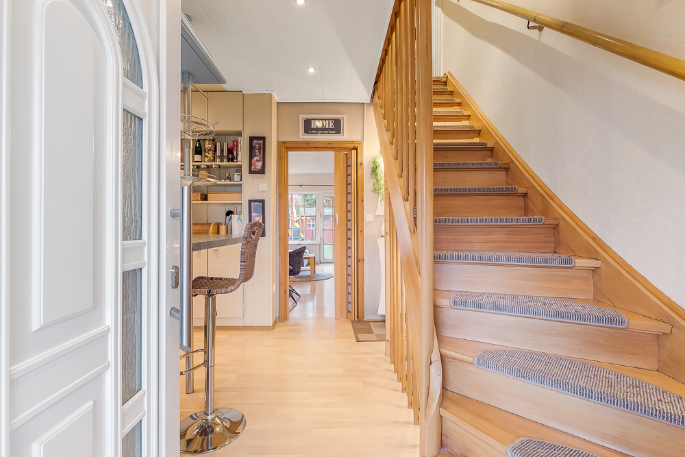Flur mit Holztreppe, Bartheke mit Hocker und Blick in ein Wohnzimmer.