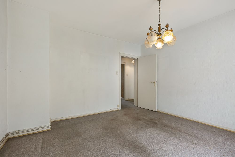 Leerer Raum mit Teppichboden, weiß gestrichenen Wänden und Kronleuchter an der Decke.