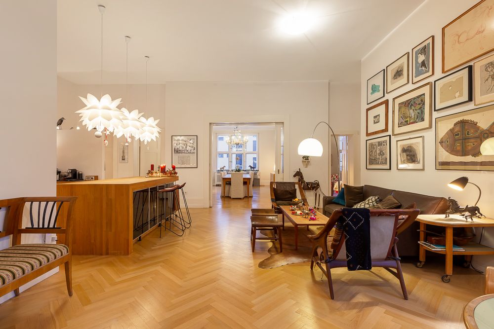 Helles Wohnzimmer mit Holzfußboden, Sitzgruppe, Kunst an der Wand und großem Esstisch im Hintergrund.
