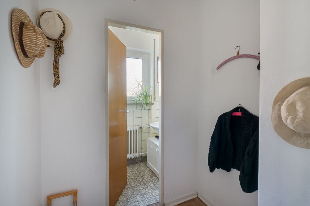 Kleiner Flur mit offenen Tür zum Badezimmer, Hüte und Jacke an den Wänden.