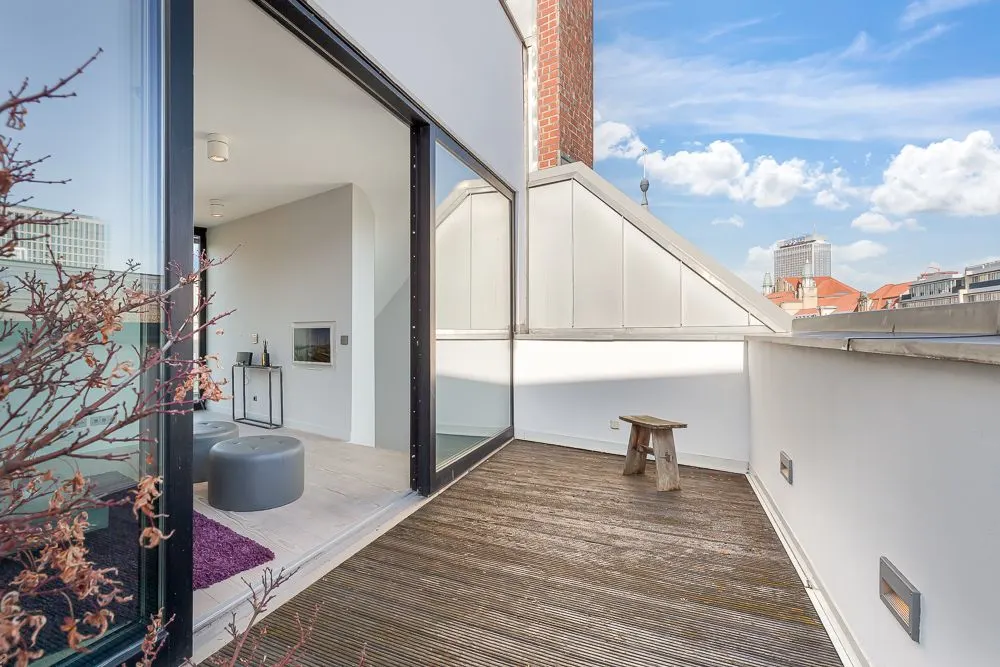 Große Dachterrasse mit Holzboden und kleinem Hocker, Zugang zu modernem Wohnzimmer.