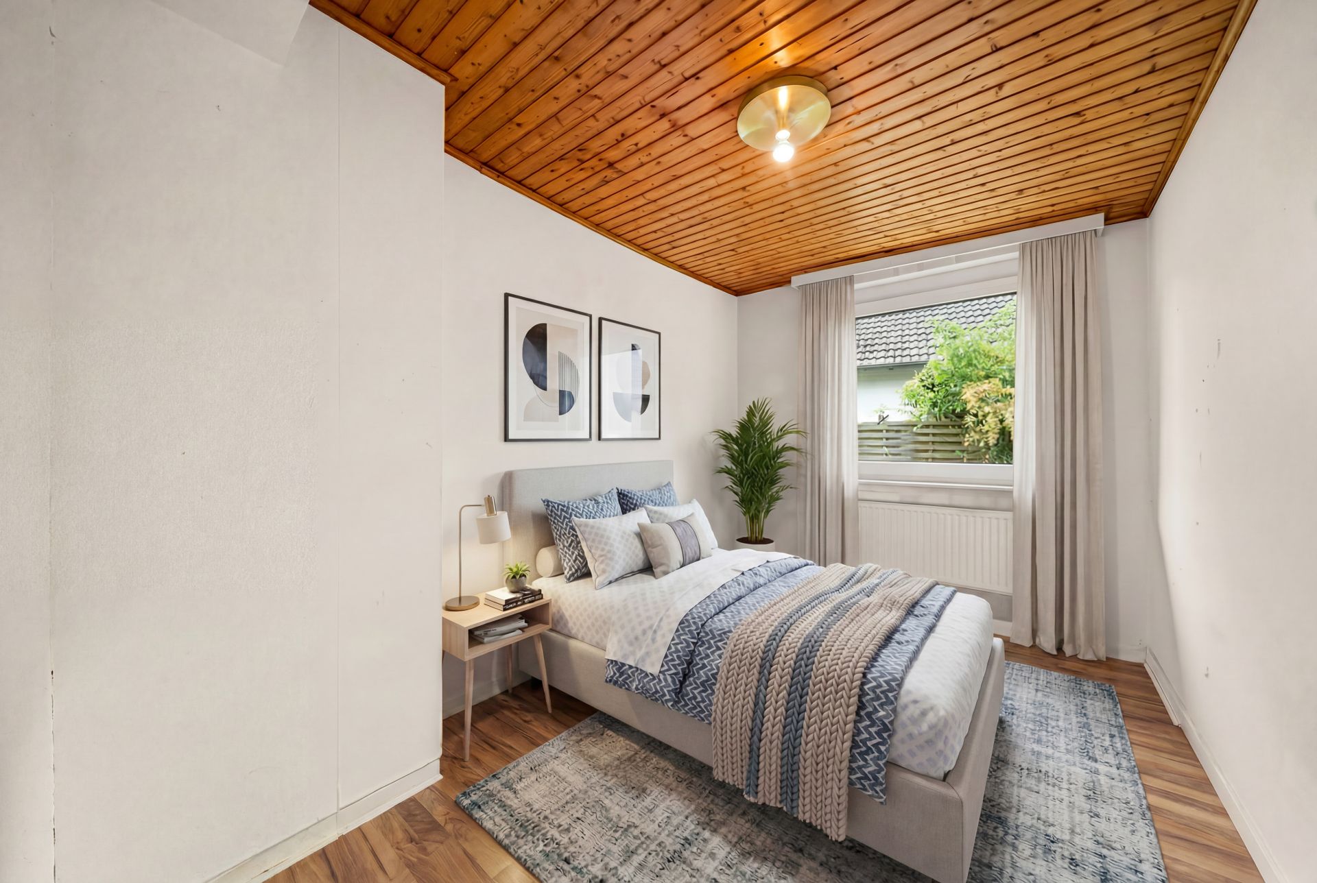 Helles Schlafzimmer mit Bett, Nachttisch, Pflanze und Holzbalkendecke.