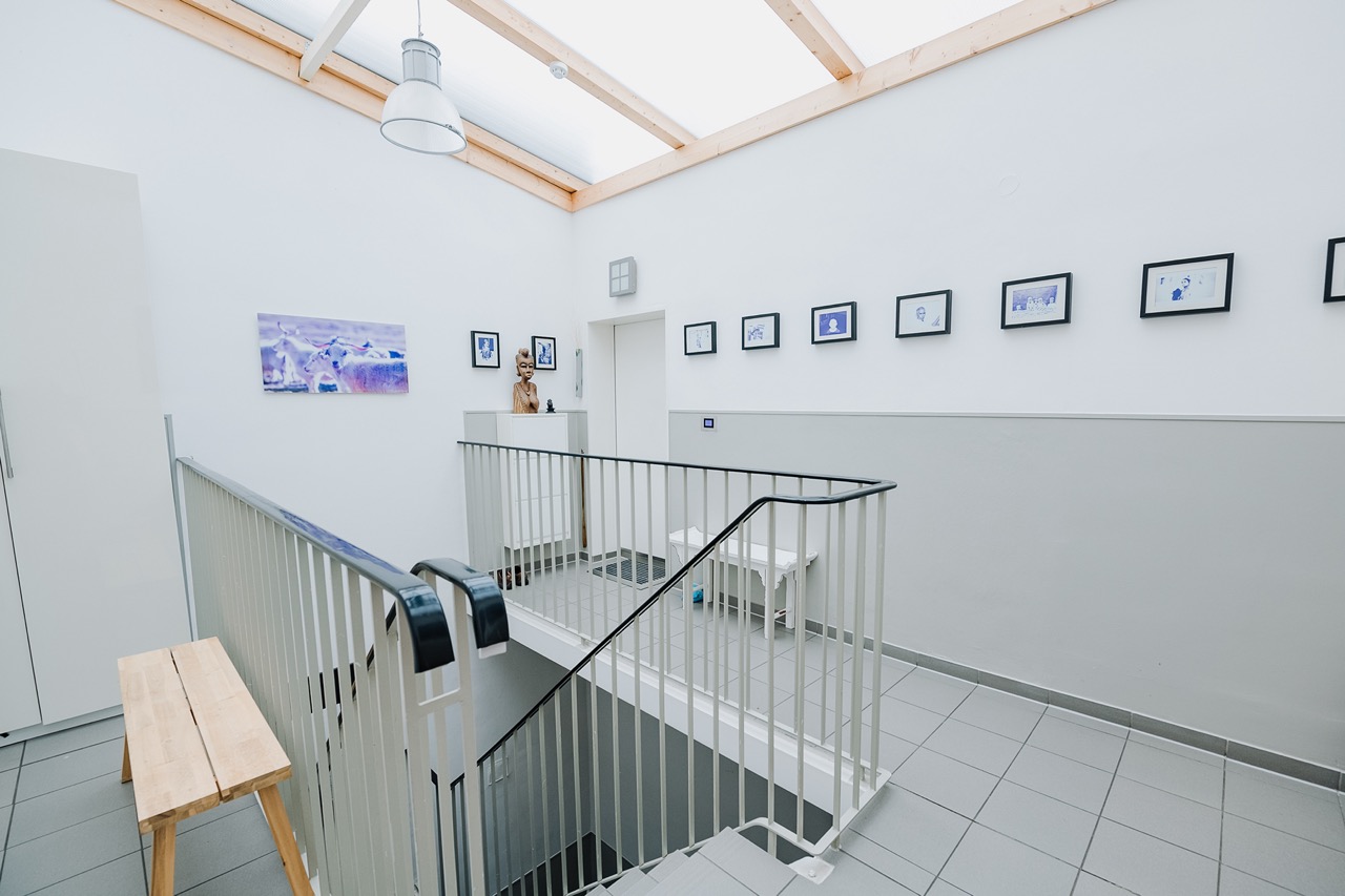 Helles Treppenhaus mit Holzbank, weißen Wänden und Bildern an der Wand.