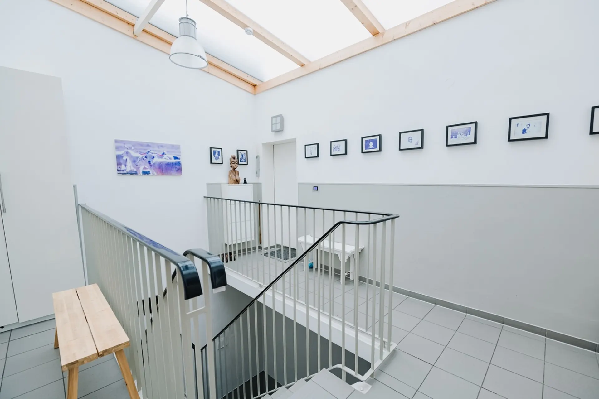 Helles Treppenhaus mit Holzbank, weißen Wänden und Bildern an der Wand.