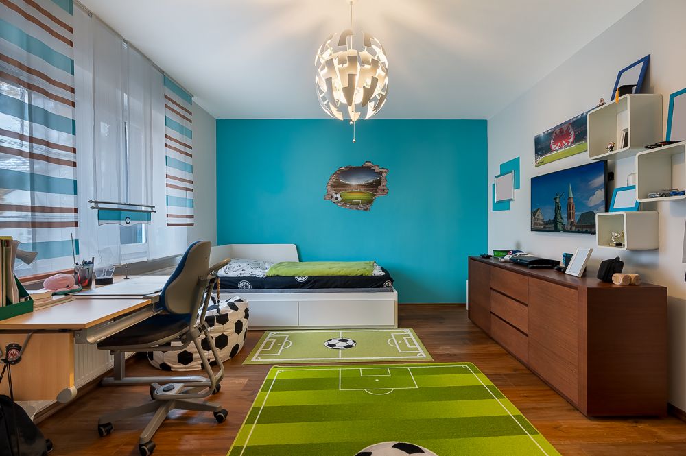 Modernes Kinderzimmer mit Fußballteppich, Schreibtisch, Bett und blauer Akzentwand.