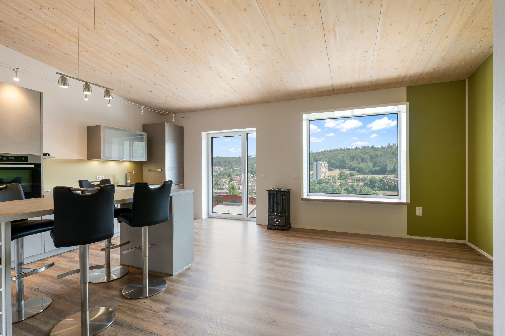 Heller Wohnraum mit Einbauküche, Holzboden, großem Fenster und Balkonzugang.