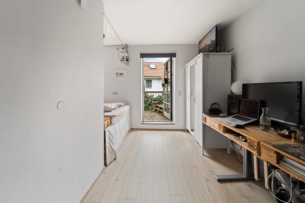 Helles Zimmer mit Bett, Schreibtisch, Schrank und Tür zu einem kleinen Balkon.