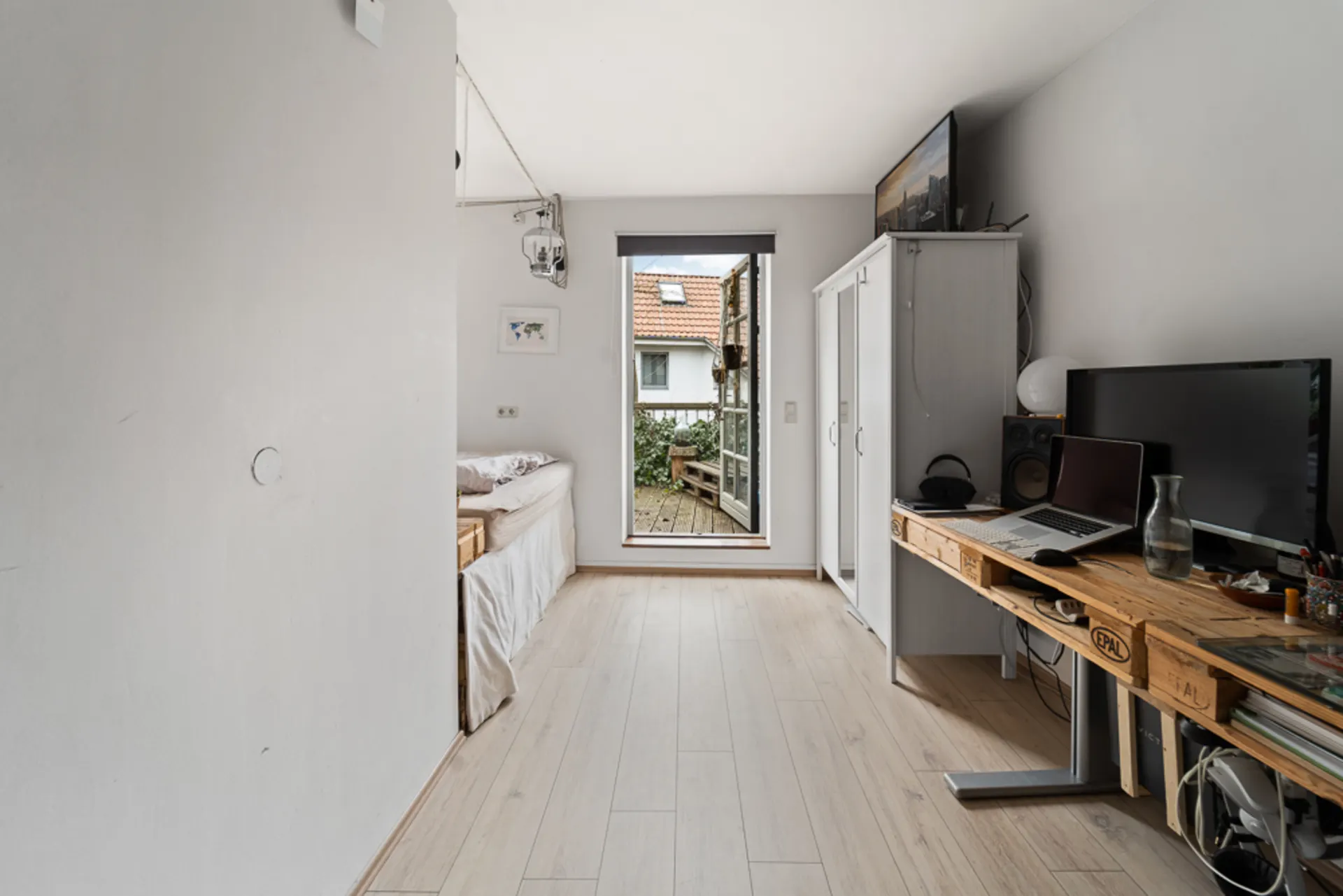 Helles Zimmer mit Bett, Schreibtisch, Schrank und Tür zu einem kleinen Balkon.