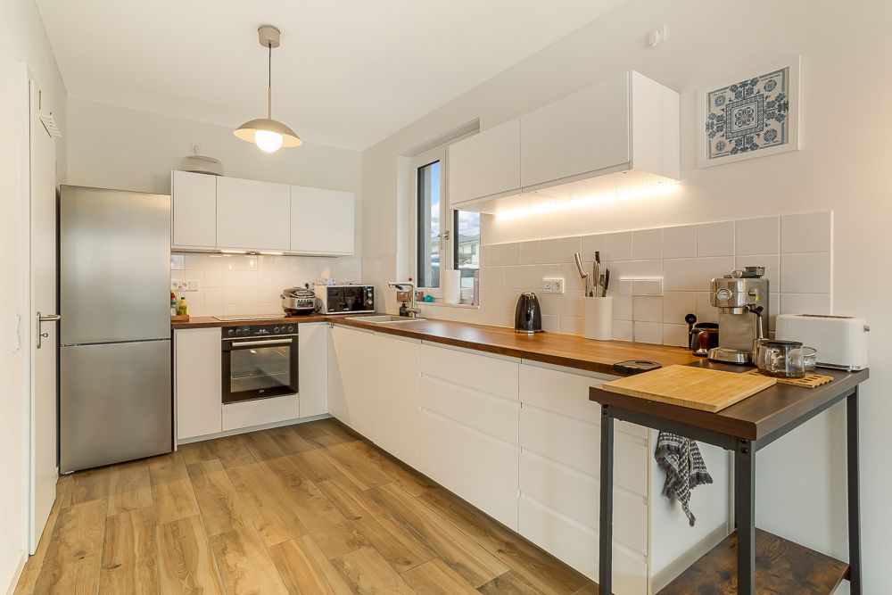 Moderne Küche mit weißen Schränken, Holzarbeitsplatte, Kühlschrank und Küchengeräten.
