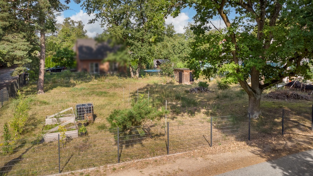 Eingezäunter Garten mit Bäumen, Hochbeeten und einem kleinen Holzschuppen.