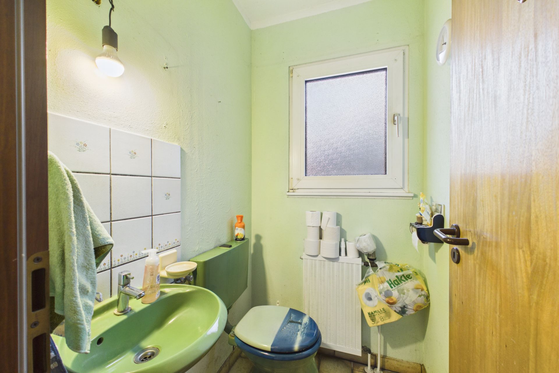 Kleines Badezimmer mit grünem Waschbecken, Toilette, Fenster und Handtuch.