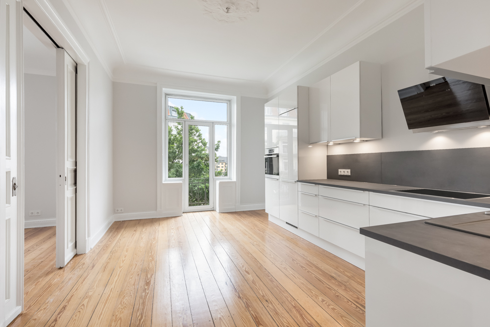 Helle, moderne Küche mit weißen Schränken, Holzfußboden und großem Fenster zur Terrasse.