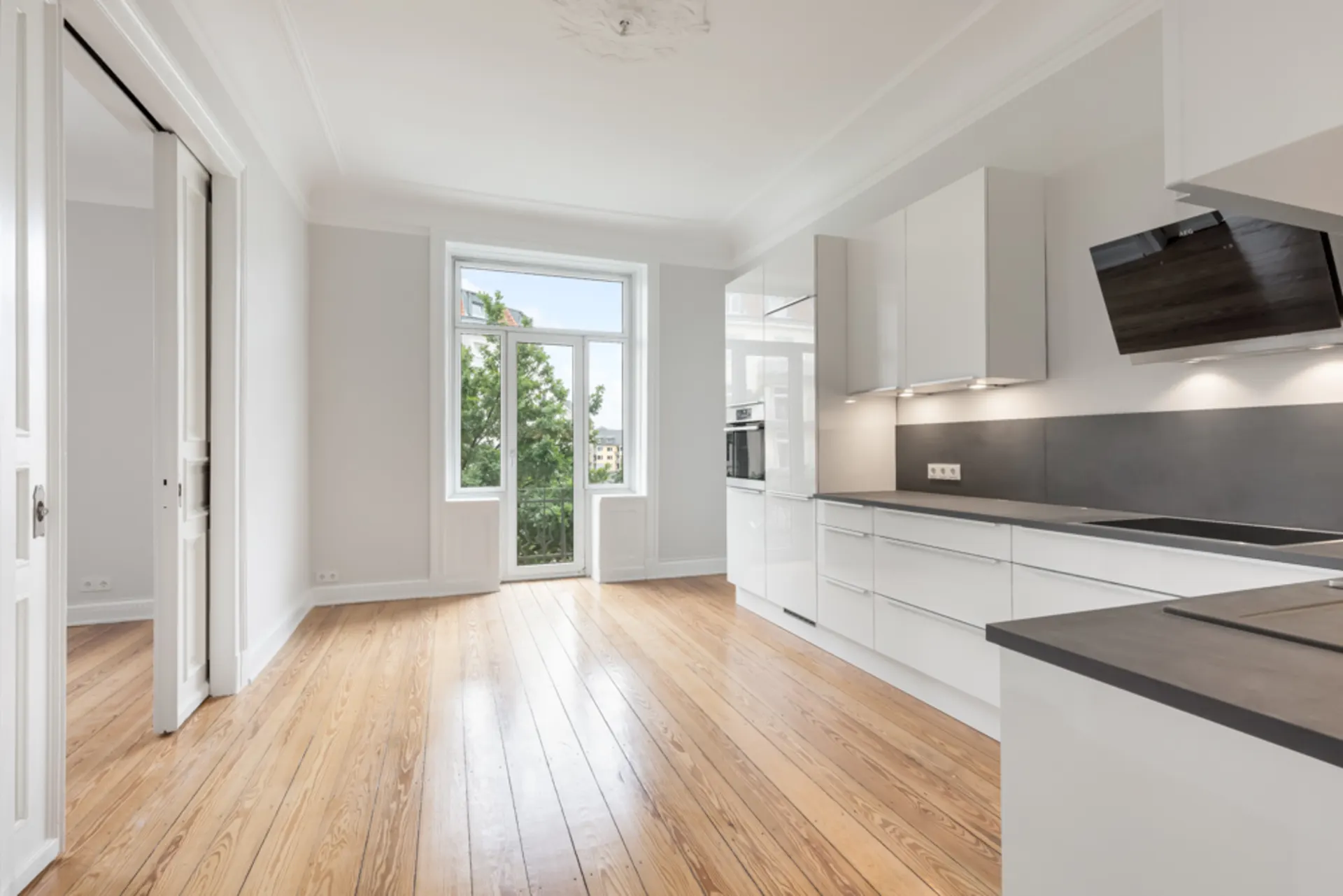 Helle, moderne Küche mit weißen Schränken, Holzfußboden und großem Fenster zur Terrasse.