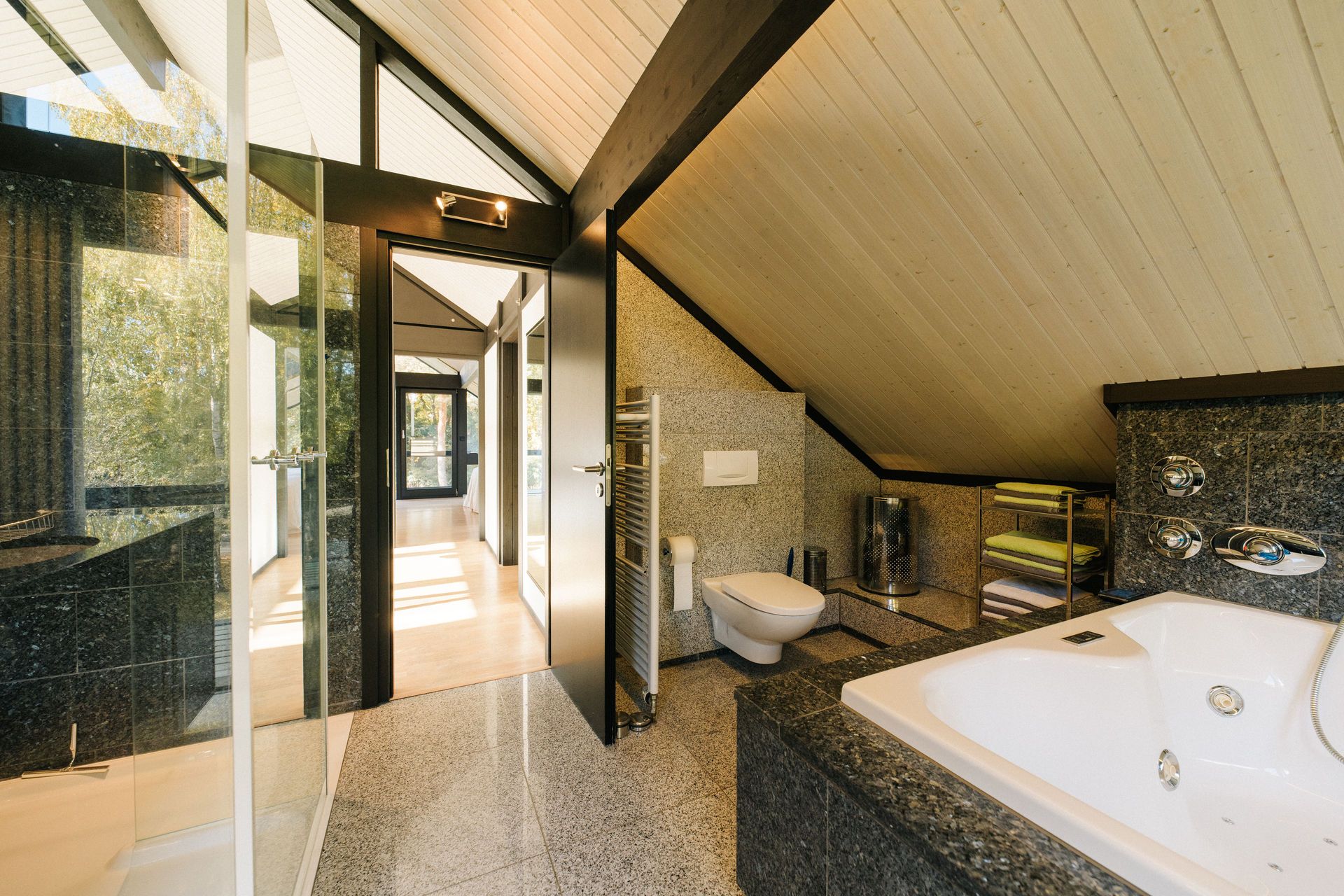 Modernes Badezimmer mit Badewanne, Dusche, WC und Dachschräge, daneben ein Flur mit viel Tageslicht.