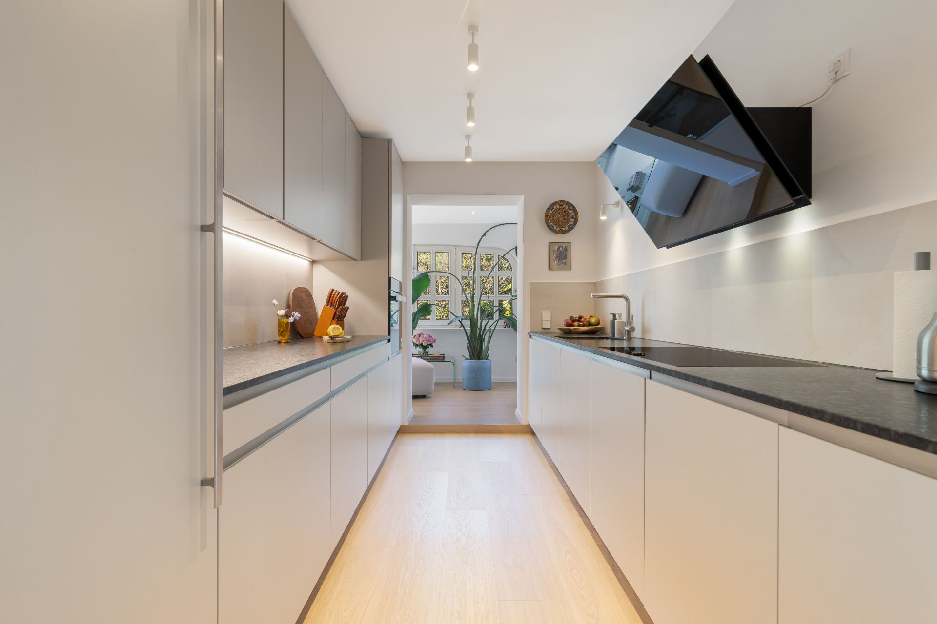 Moderne Küche mit hellen Schränken, schwarzer Arbeitsplatte und Blick ins Wohnzimmer.