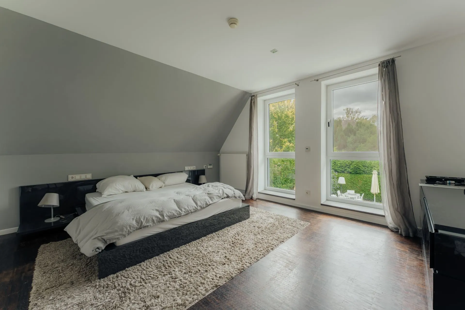 Helles Schlafzimmer mit großem Bett, Teppich, Fenstern und dunklem Holzboden.