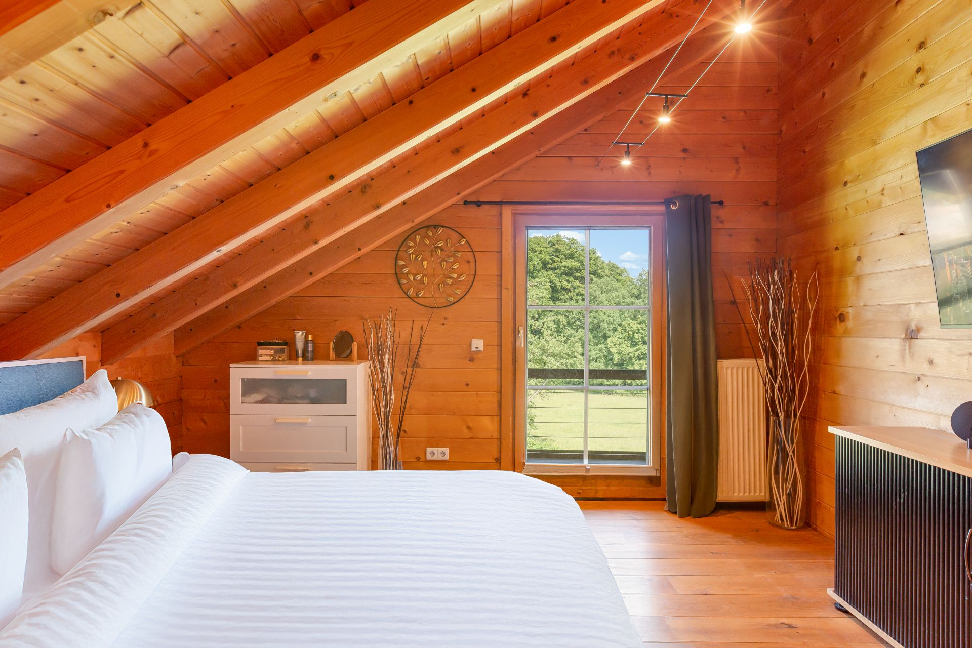 Schlafzimmer im Dachgeschoss mit Holzverkleidung, Bett, Kommode und Fenster mit Ausblick ins Grüne.