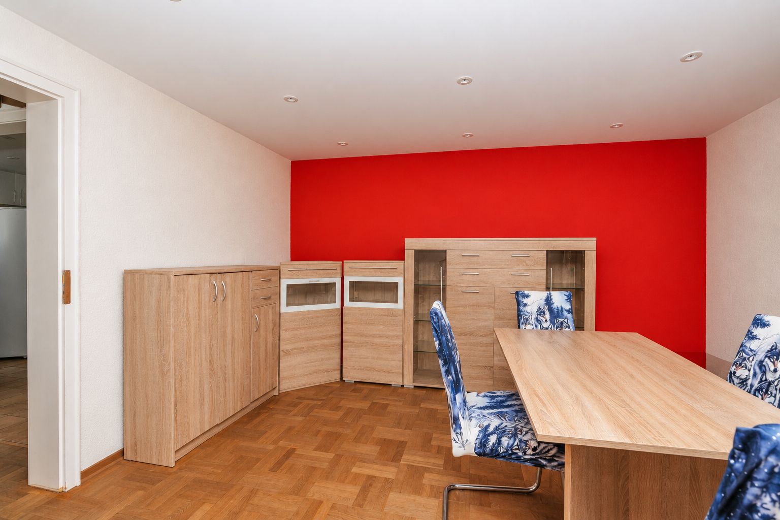 Raum mit Holzmöbeln, blau gemusterten Stühlen und roter Wand.