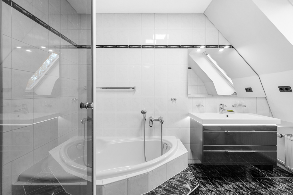 Modernes Badezimmer mit Eckbadewanne, Waschbecken, Spiegel und Fenster im Dachgeschoss.