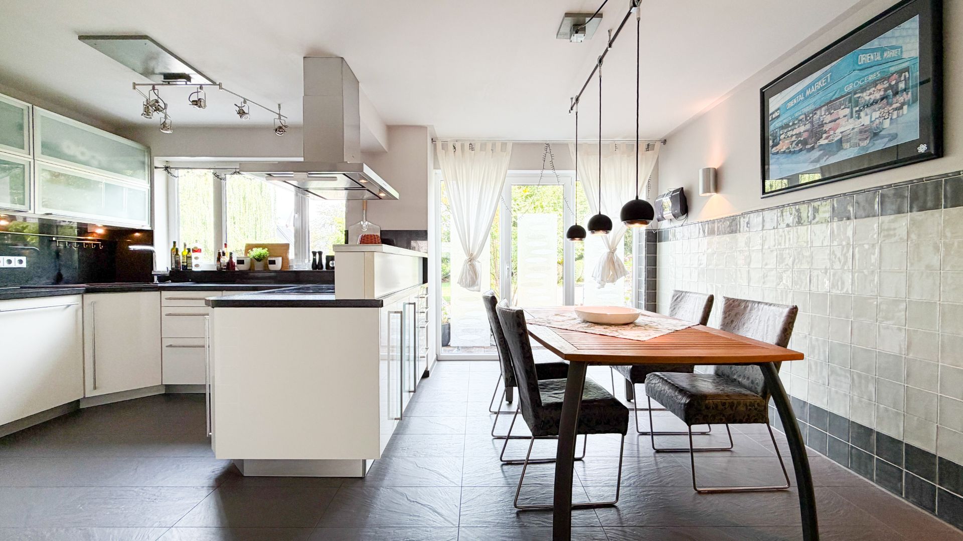 Moderne Küche mit Esstisch, vier Stühlen und großen Fenstern, die auf eine Terrasse führen.