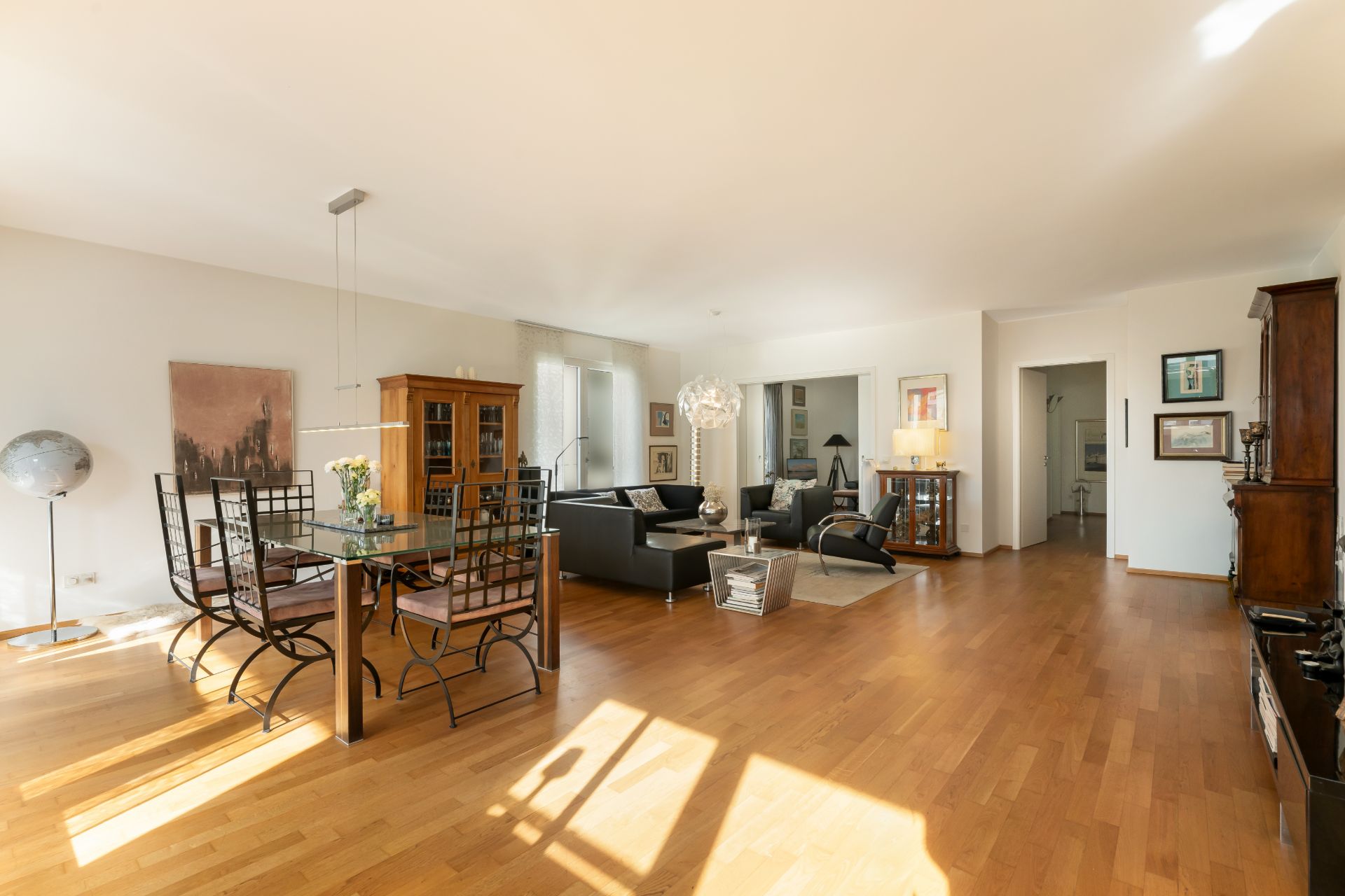 Helles Wohnzimmer mit Holzboden, Esstisch, schwarzen Stühlen und Sitzecke mit Sofas.