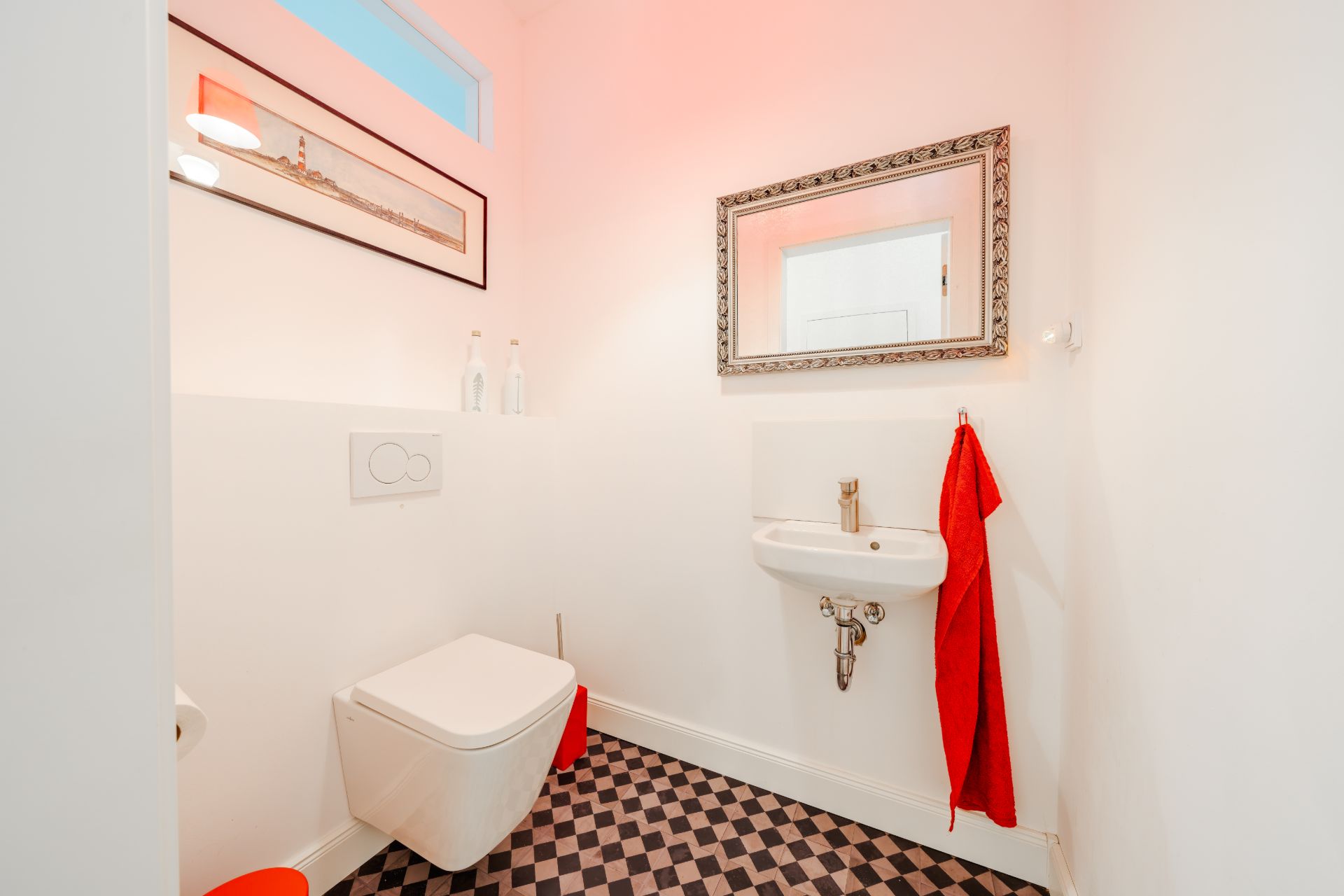Kleines Bad mit Wandtoilette, Waschbecken, Spiegel und rot kariertem Handtuch auf kariertem Boden.