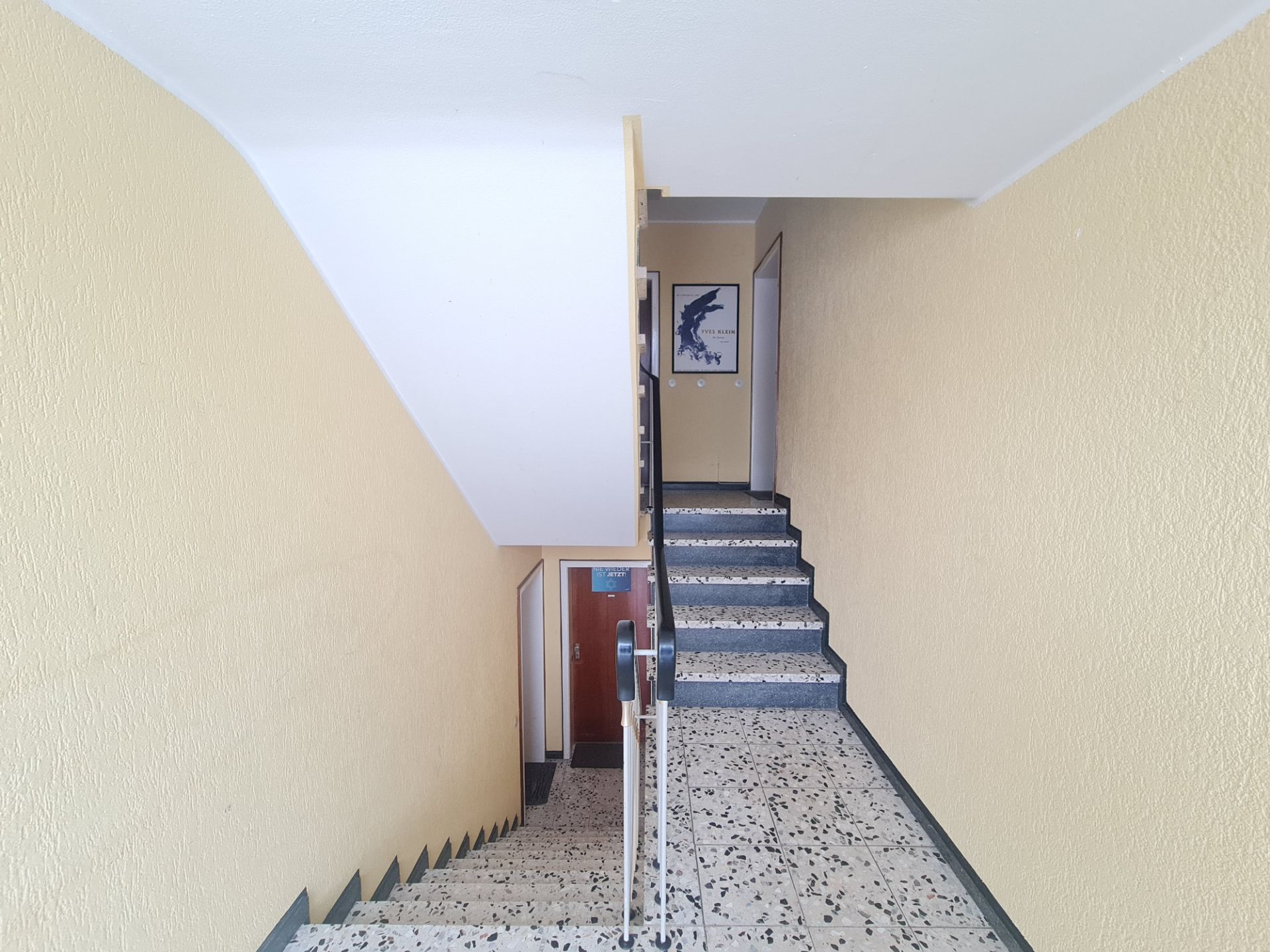Treppenhaus mit gelben Wänden, gelbem Handlauf und einer Tür am oberen Ende.