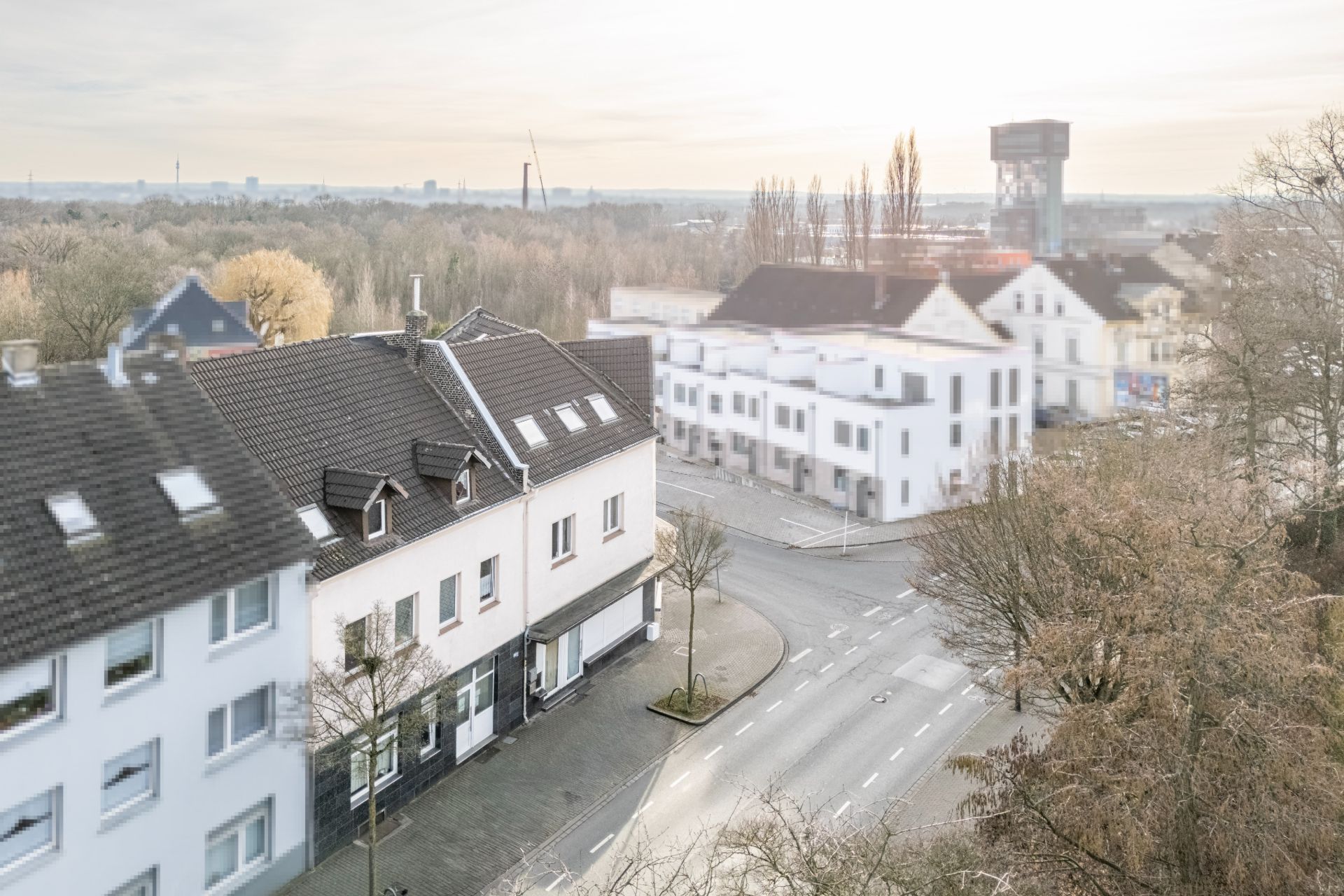 Blick auf eine Straßenecke mit mehreren Wohnhäusern und Bäumen bei Tageslicht.