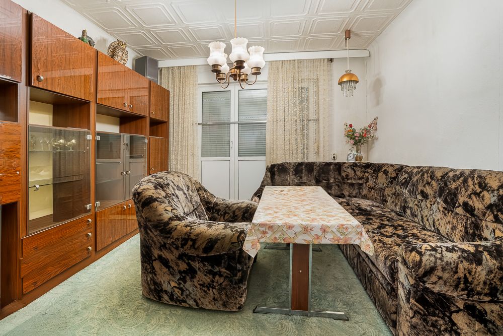 Wohnzimmer mit Ecksofa, Sessel, Holzwandschrank, Esstisch und Deckenleuchte.