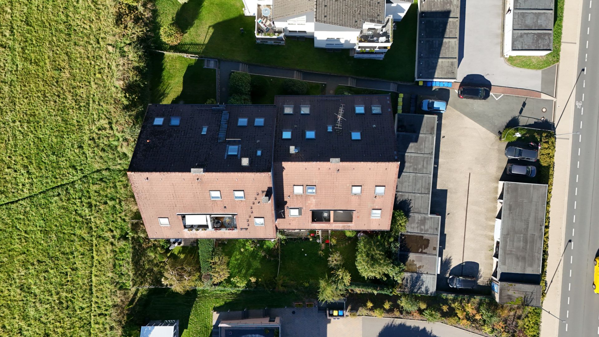 Luftaufnahme eines Wohnhauses mit Garten, umgeben von Parkplätzen und einer Straße.