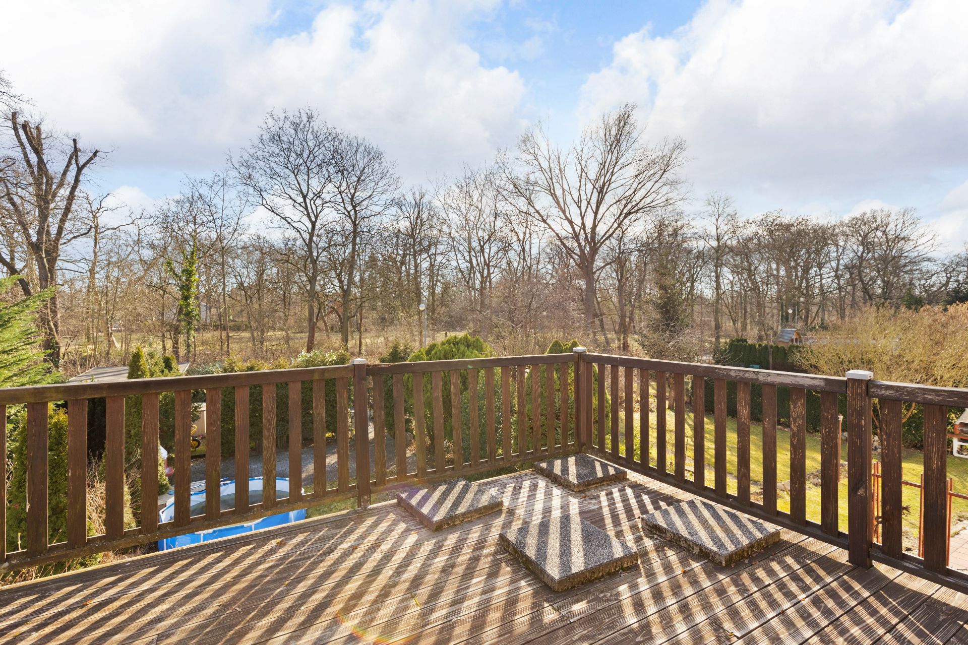 Holzbalkon mit Stufen und Ausblick auf Garten und Bäume bei Tageslicht.