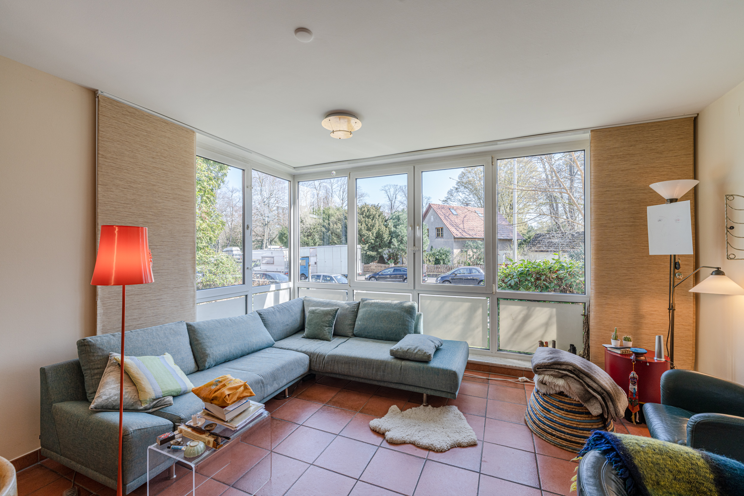 Helles Wohnzimmer mit Ecksofa, großen Fenstern, roten Fliesen und mehreren Stehlampen.