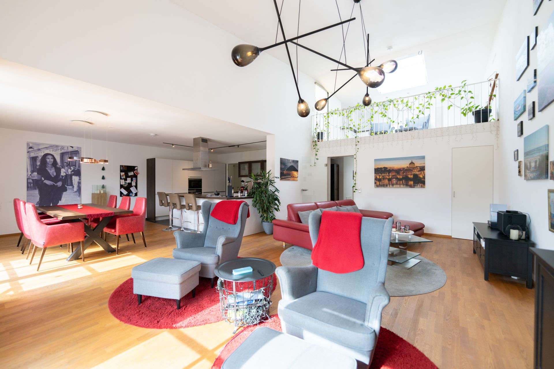 Helles Wohnzimmer mit roten Sesseln, Esstisch, moderner Küche und großen Fenstern.