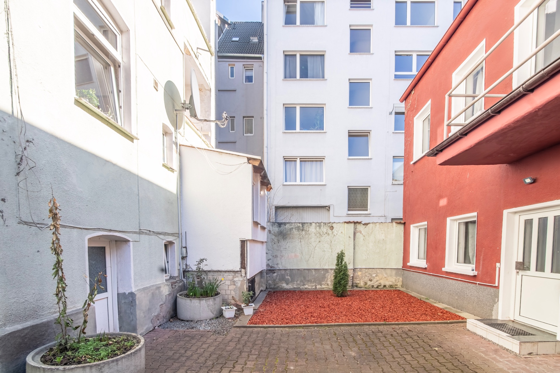 Gepflasterter Innenhof mit Pflanzkübeln, rotem Kies und umliegenden Wohngebäuden.