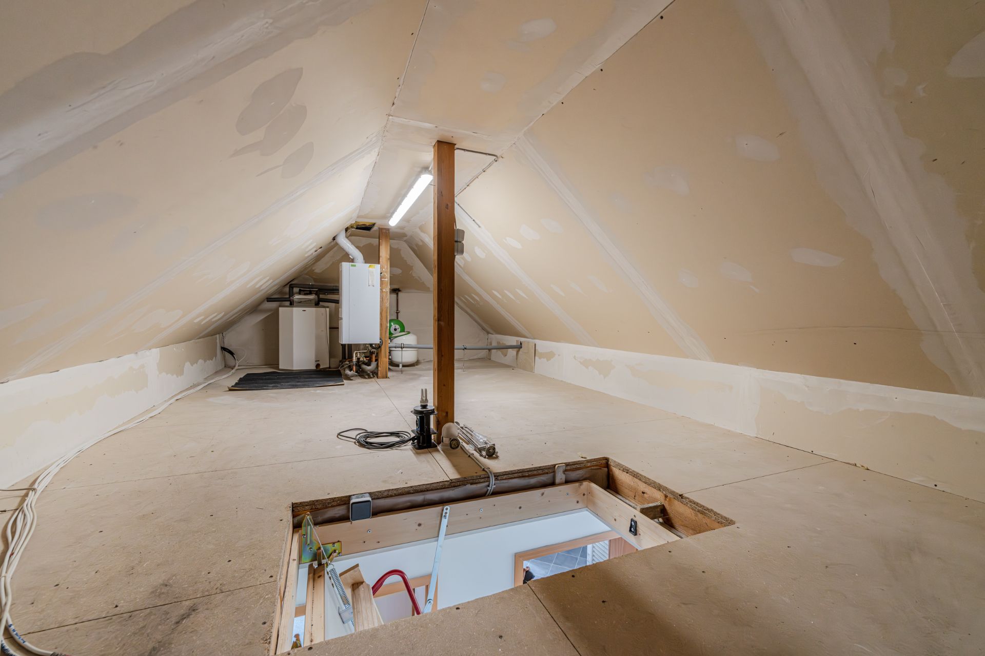 Unausgebauter Dachboden mit schrägen Wänden, Heizungsanlage und einer Öffnung im Boden.