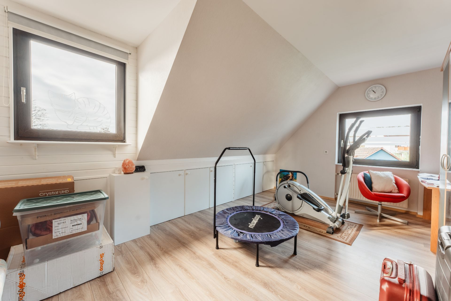 Heller Raum mit Fitnessgerät, Trampolin, rotem Stuhl und zwei Fenstern im Dachgeschoss.